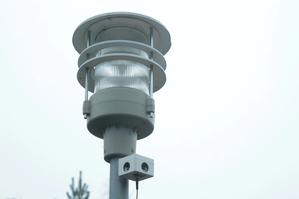 Odstraszacz ultradźwiękowy zamontowany pod nowoczesną lampą ogrodową na słupku, skierowany w dół.