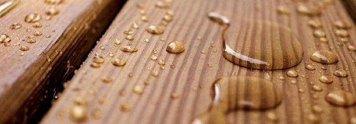 Krople wody na drewnianej powierzchni, ukazujące efekt hydrofobowy desek.