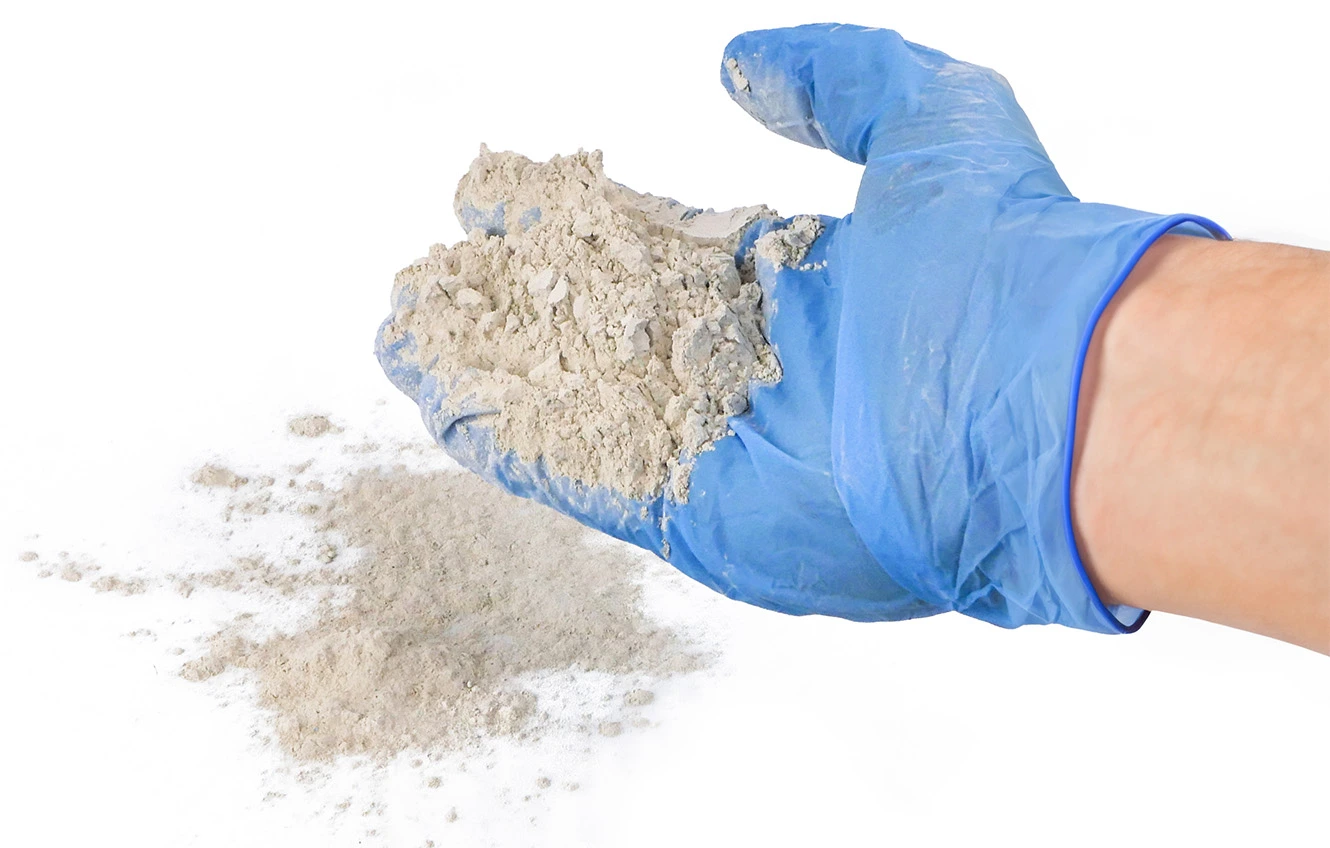 Osoba w niebieskiej rękawiczce rozsypująca beżowy proszek do dezynfekcji.